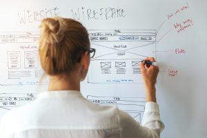 How much does a website cost | Person writing on whiteboard with website design layout.